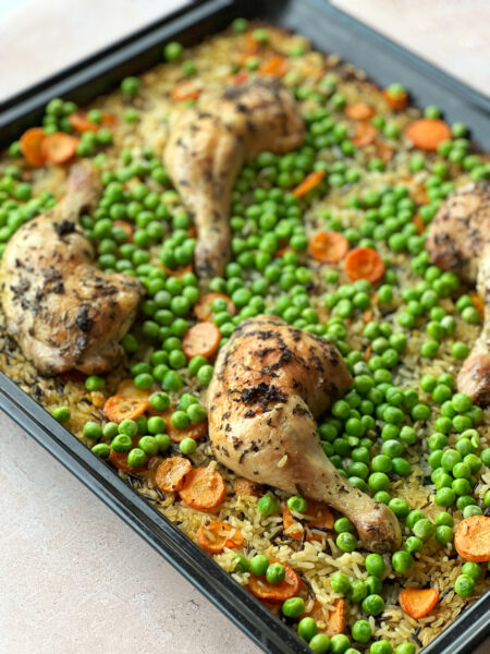 Pouletschenkel aus dem Ofen mit Reis und Gemüse auf einem Teller auf einem Backblech