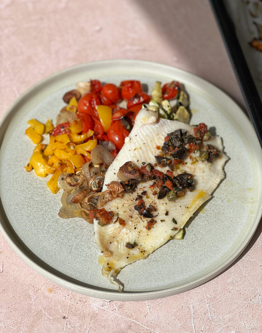 Fisch vom Blech mit mediterranem Gemüse serviert auf einem Teller.