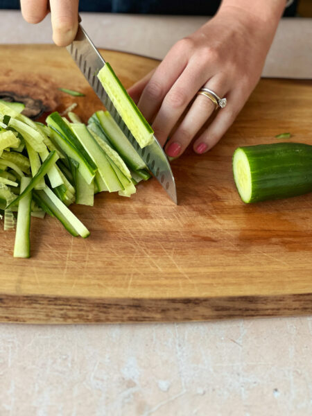 Gurke und Karotten in ca. 5 cm lange Stifte schneiden. Bundzwiebel in feine Ringe schneiden. Mit den Edamame auf den Glasnudeln verteilen.
