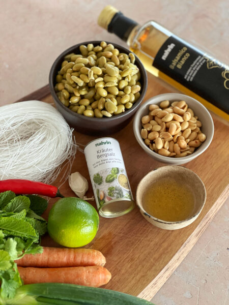 Zutaten: Glasnudeln Gurke & Karotten Gekochte Edamame-Bohnen ohne Schale; alternativ kannst du auch gebratenen Tofu als Proteinquelle in den Glasnudelsalat geben Bundzwiebel Knoblauchzehe Chilischote Sesamöl Kräuter Bergsalz von Nahrin Balsamico Bianco von Nahrin Frischer Koriander & Pfefferminz Limette und Erdnüsse zum Garnieren