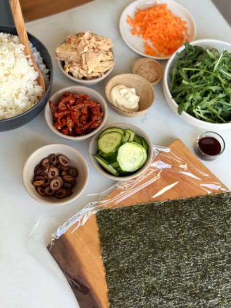 Den Reis mit 400 ml Wasser in einem Topf kochen (Seite 10). Thunfisch abtropfen lassen und in einer kleinen Schüssel mit Mayonnaise und Sojasauce vermengen. Die Gurke in dünne Scheiben schneiden. Oliven in Scheiben schneiden, Tomaten abtropfen lassen und je nach Grösse halbieren oder dritteln. Den Rucola waschen und trocken schütteln. Die Möhre schälen und mit dem Sparschäler in dünne Streifen schneiden. Ein Nori-Blatt mit der Spitze nach unten auf ein Schneidbrett legen. Den Reis in einem Quadrat (10 x 10 cm) 1 cm dick darauf verteilen. Leicht salzen. Den Belag auf den Reis schichten. Mit einer zweiten Reisschicht bedecken und erneut leicht salzen. Das Nori-Blatt wie einen Briefumschlag über dem Reis falten und schliessen. In Frischhaltefolie wickeln und 10 Minuten ruhen lassen. Einmal durchschneiden und geniessen.