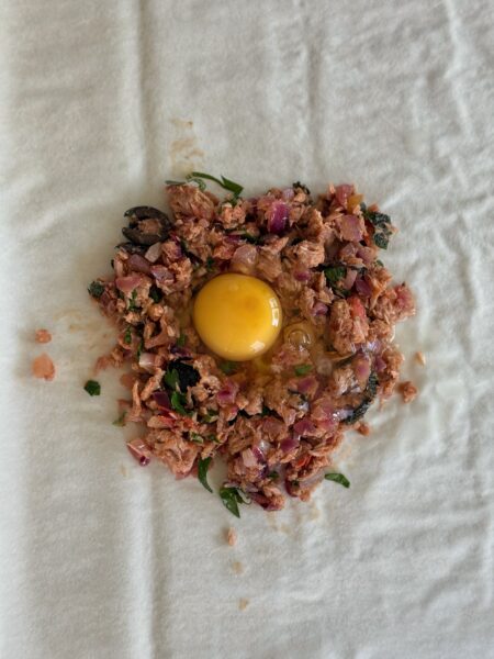 Die Zwiebeln schälen und fein hacken. Die Tomate in kleine Würfel schneiden und die Oliven halbieren. Die Butter in einer Pfanne aufschäumen. Zwiebeln und die Tomate hineingeben und anschwitzen. Den abgetropften Thunfisch in eine Schüssel geben. Die Zwiebel-Tomaten-Mischung, die halbierten Oliven sowie Minze, Petersilie und Ras el-Hanout hinzufügen und alles gleichmässig vermengen, mit Salz und Pfeffer abschmecken.