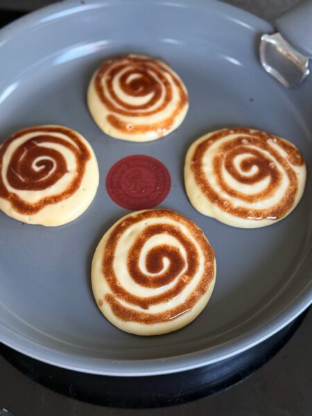 Zubereitung ✨ 1. Zimt-Swirl vorbereiten: Butter schmelzen und mit Zimt, Zucker und Premium Vanilleextrakt von Dr. Oetker gründlich verrühren. Die Mischung in einen Spritzbeutel mit kleiner Öffnung füllen und zur Seite stellen. 2. Mehl, Backpulver, Salz und Zucker vermischen. Buttermilch und Eier dazugeben und zu einem glatten Teig verrühren, aber nicht zu lange rühren. 3. Pancakes backen: Etwas Butter in einer Pfanne bei mittlerer Hitze zerlassen. Für jeden Pancake Teig hineingeben (ca. 8 cm Ø). Nach 1–2 Minuten mit dem Spritzbeutel den Zimt-Swirl spiralförmig von aussen nach innen auf den noch feuchten Teig geben. Pancake fertig backen lassen, nicht wenden. Warm stellen.