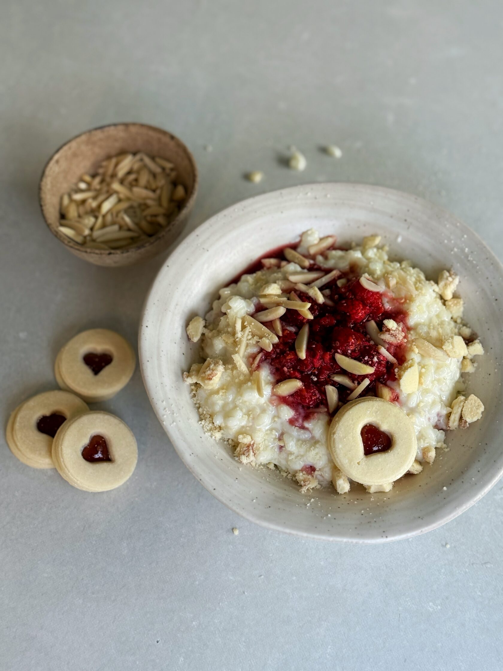 Die Milch in einem Topf langsam erhitzen, bis sie fast kocht. Den Reis hinzufügen, die Hitze reduzieren und den Milchreis bei schwacher Hitze unter häufigem Rühren etwa 25-30 Minuten köcheln lassen, bis der Reis weich ist und der Brei cremig wird. Dabei darauf achten, dass die Milch nicht überkocht oder anbrennt. Himbeeren mit Ahornsirup kurz aufkochen und kurz köcheln, ca. 2 min. Warmer Milchreis auf zwei Schüsseln verteilen und kleine Mulden in der Mitte eindrücken. Himbeeren direkt heiss in die Mulde leeren, Spitzbuben Guetzli zerbröckeln und darüberstreuen und mit Mandeln servieren.