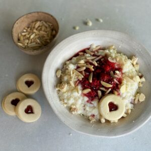 Die Milch in einem Topf langsam erhitzen, bis sie fast kocht. Den Reis hinzufügen, die Hitze reduzieren und den Milchreis bei schwacher Hitze unter häufigem Rühren etwa 25-30 Minuten köcheln lassen, bis der Reis weich ist und der Brei cremig wird. Dabei darauf achten, dass die Milch nicht überkocht oder anbrennt. Himbeeren mit Ahornsirup kurz aufkochen und kurz köcheln, ca. 2 min. Warmer Milchreis auf zwei Schüsseln verteilen und kleine Mulden in der Mitte eindrücken. Himbeeren direkt heiss in die Mulde leeren, Spitzbuben Guetzli zerbröckeln und darüberstreuen und mit Mandeln servieren.