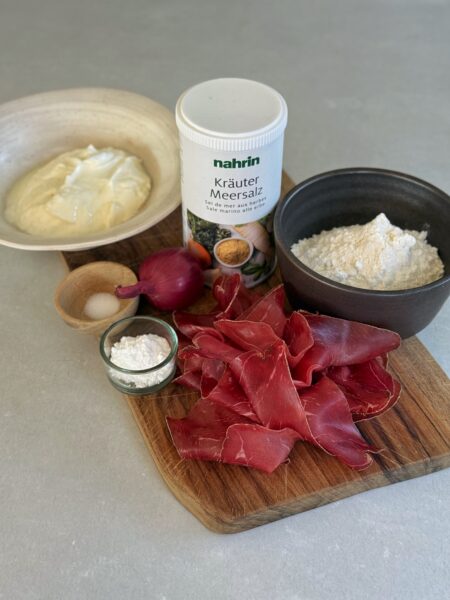 130 g Magerquark 80 g Weissmehl 1 TL Backpulver 1/4 TL Salz Zutaten für den Belag 100 g Magerquark 80 g Bündnerfleisch oder Hobelfleisch 1 Zwiebel ½ TL Kräuter Meersalz von Nahrin